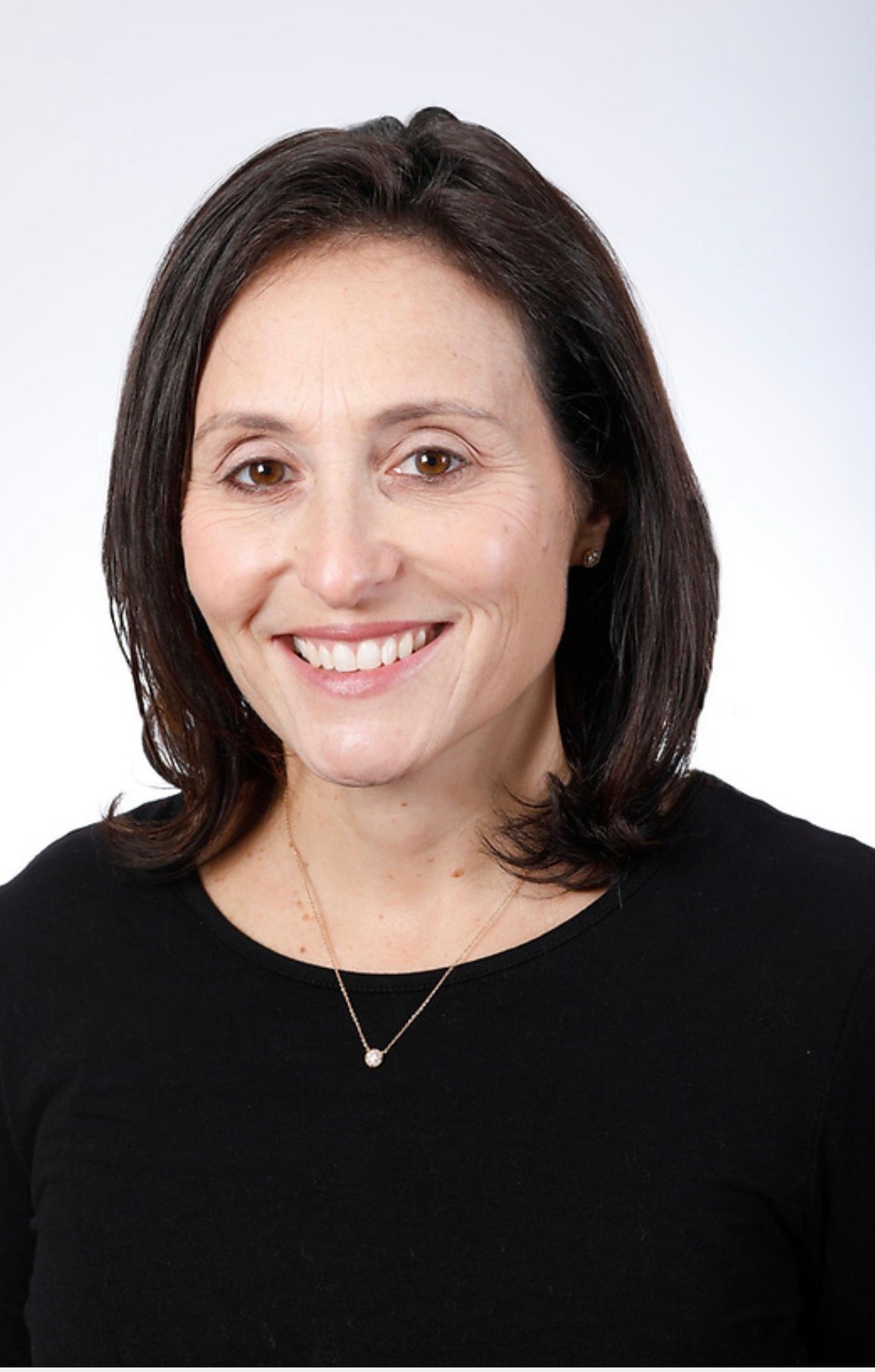 Alison Freedman, smiling, in a black top against a white studio background.